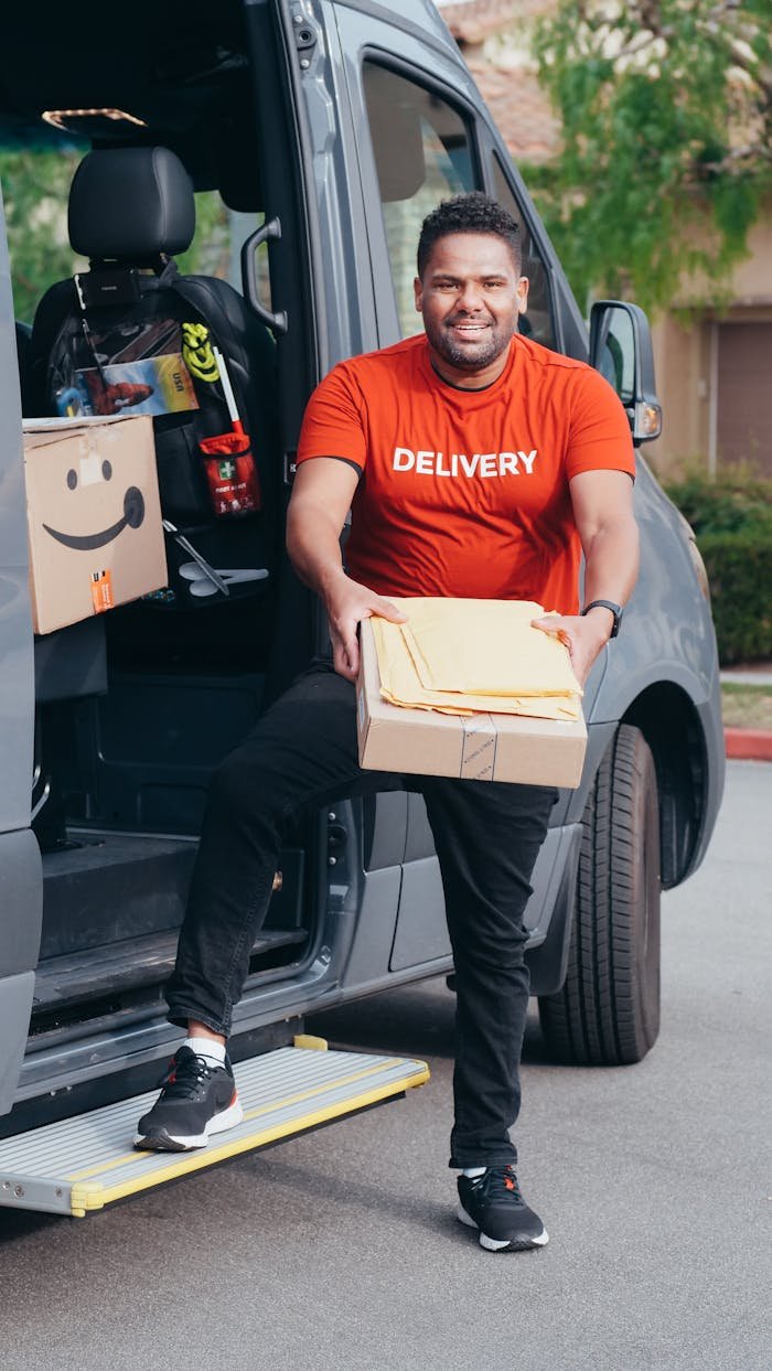 Contacto paquetería Badalona. Happy delivery man stepping out of van holding a package.